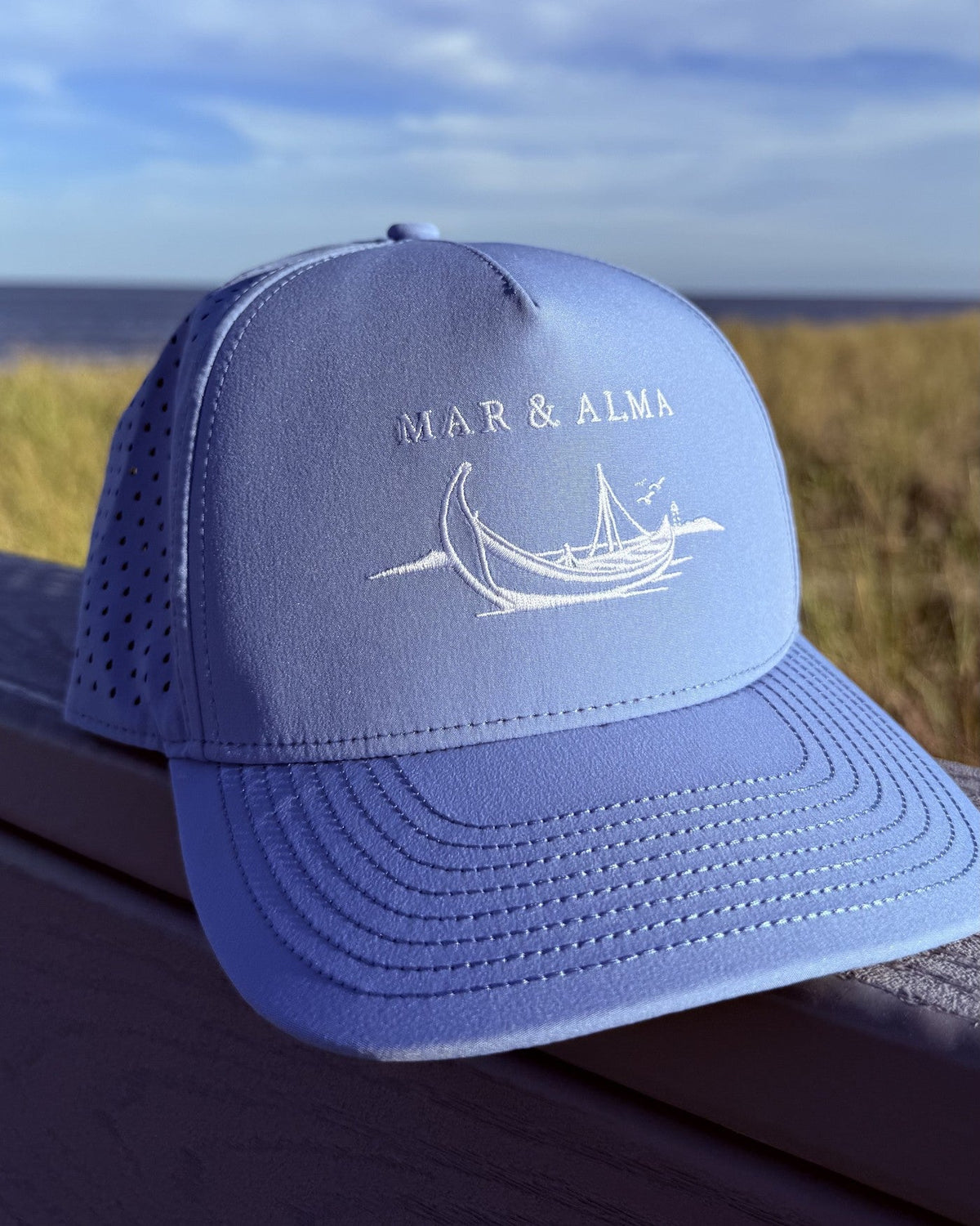 The teen fit snapback on a boardwalk rail, dune grass and the Atlantic behind.