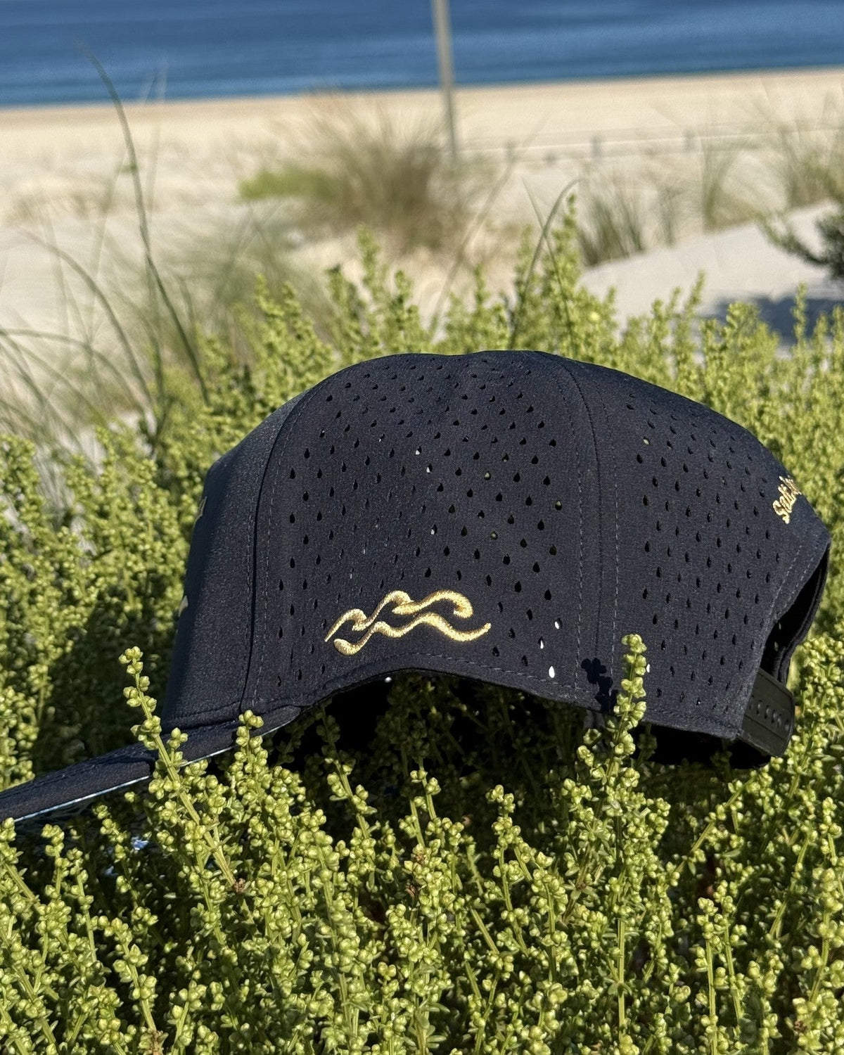 The side of the navy snapback, the gold wave mark above the laser cut perforations.