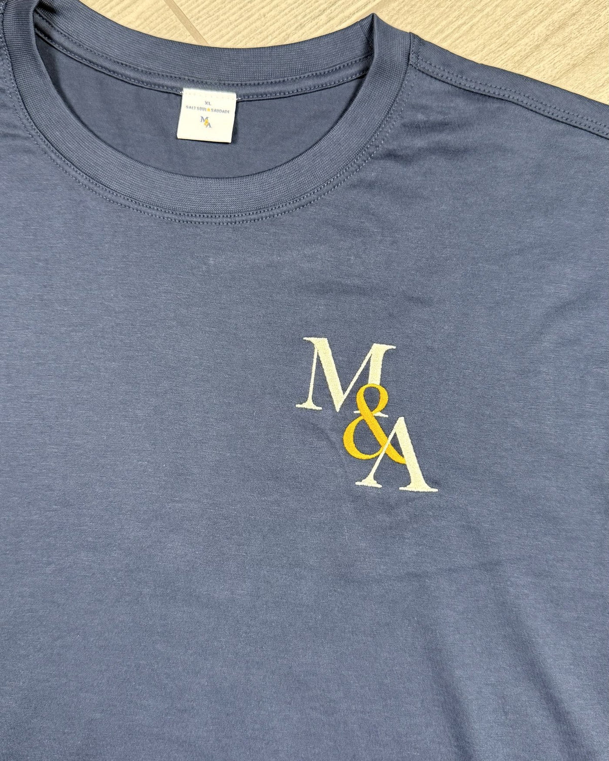 Macro of the M&A monogram in gold and white, stitched on navy.